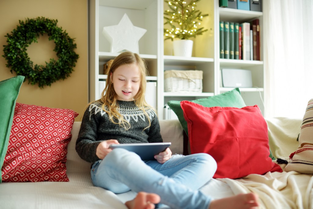 Cute young daughter having online video call on Christmas time. Chatting with distant family during pandemic. Staying safe during winter holidays. Christmas celebration using modern gadgets.
