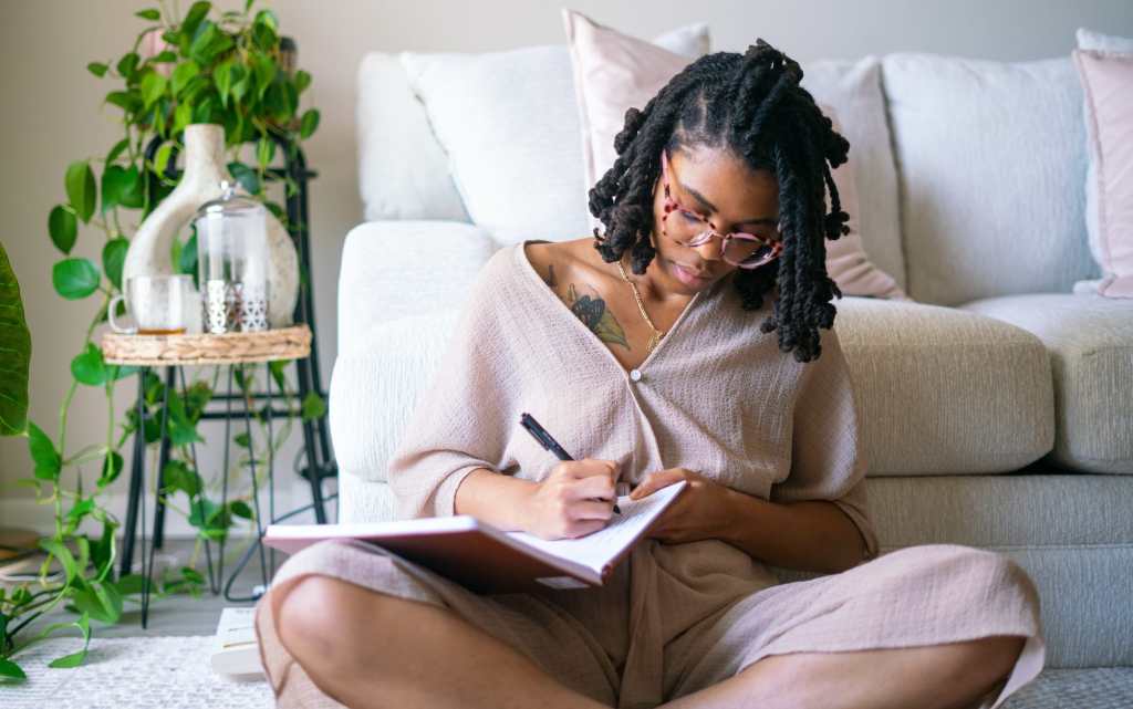 black woman writing in a journal at home surrounded by plants